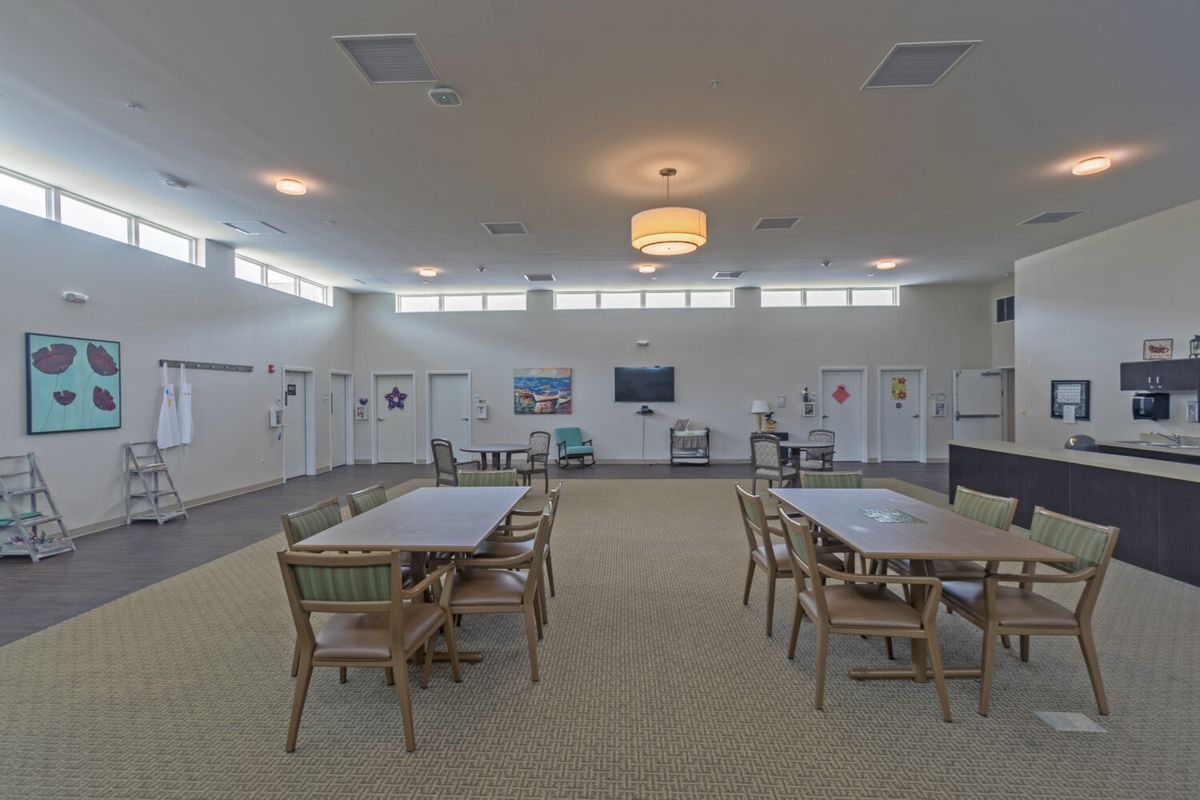 A spacious and well-lit interior room featuring tables and chairs, with a television on the wall.