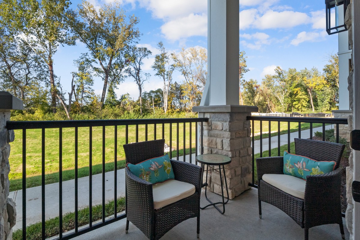A cozy patio with outdoor chairs and a small table overlooking a grassy area and trees.