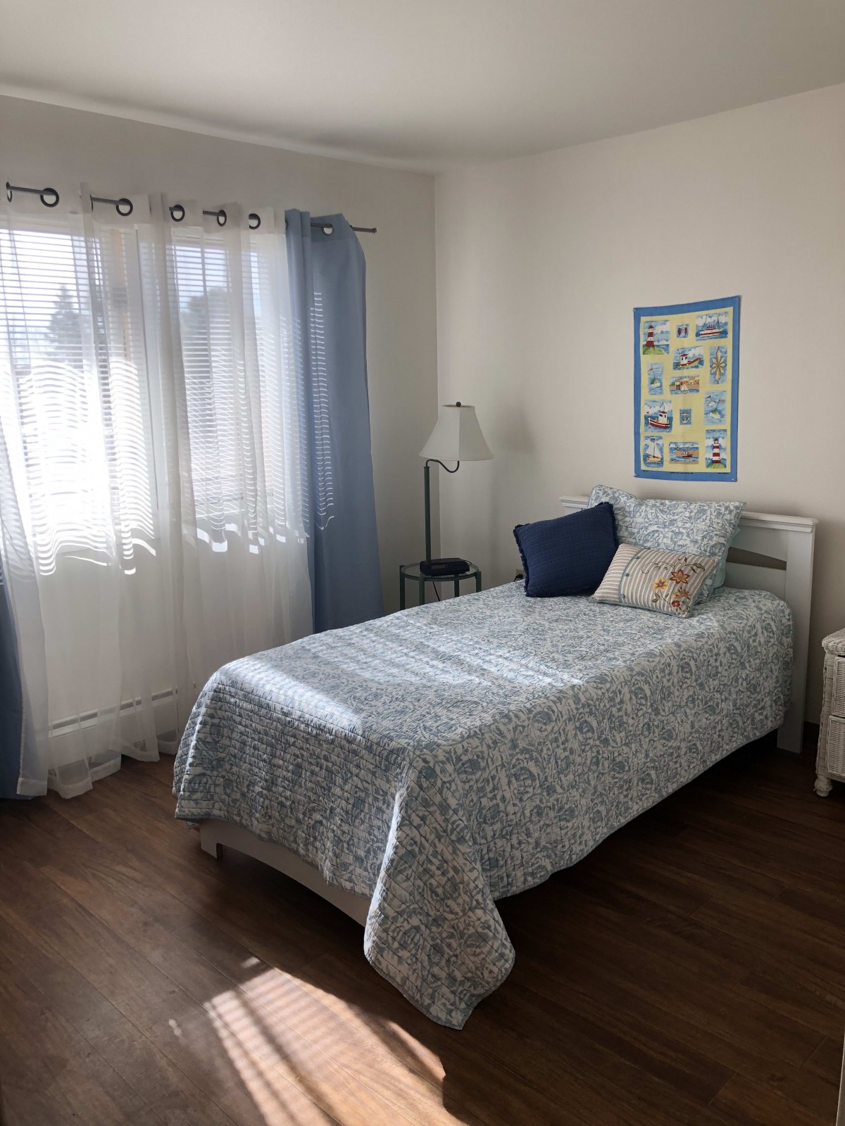 A cozy bedroom with a single bed, blue curtains, and sunlight streaming through the window.