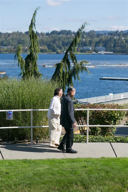 Two people walking on a path by the lake surrounded by lush greenery.
