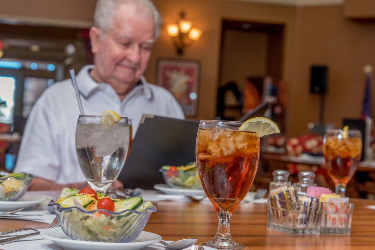 A person reading a menu at a restaurant table with drinks and salad.