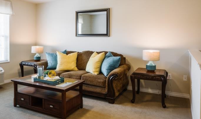 A cozy living room with a brown sofa adorned with colorful pillows, a wooden coffee table, and matching side tables with lamps.