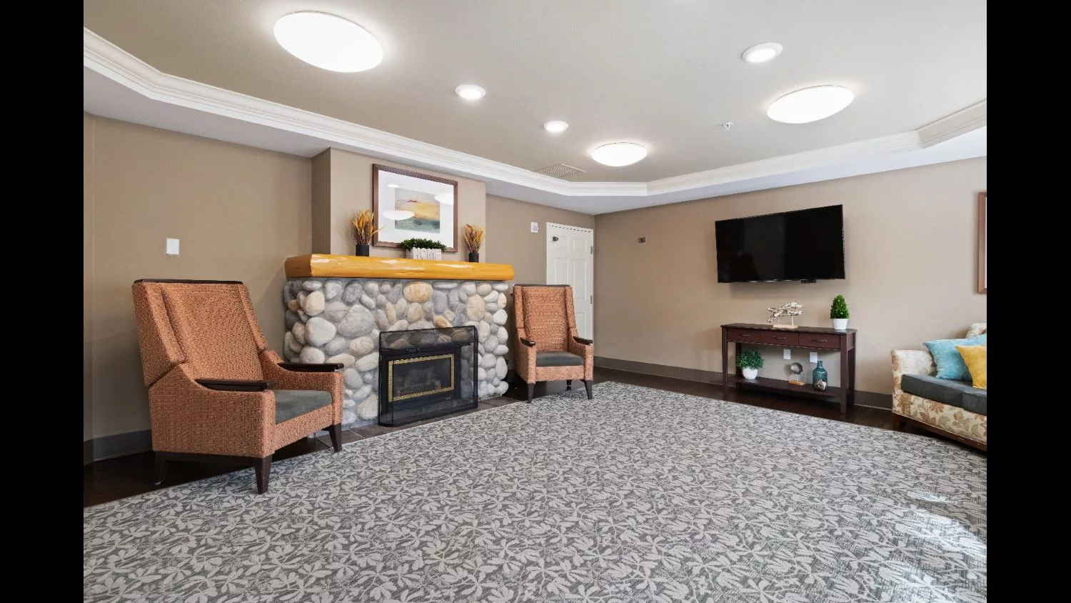 A cozy living room with a stone fireplace, comfortable seating, a large television, and decorative elements including a painting above the mantel.