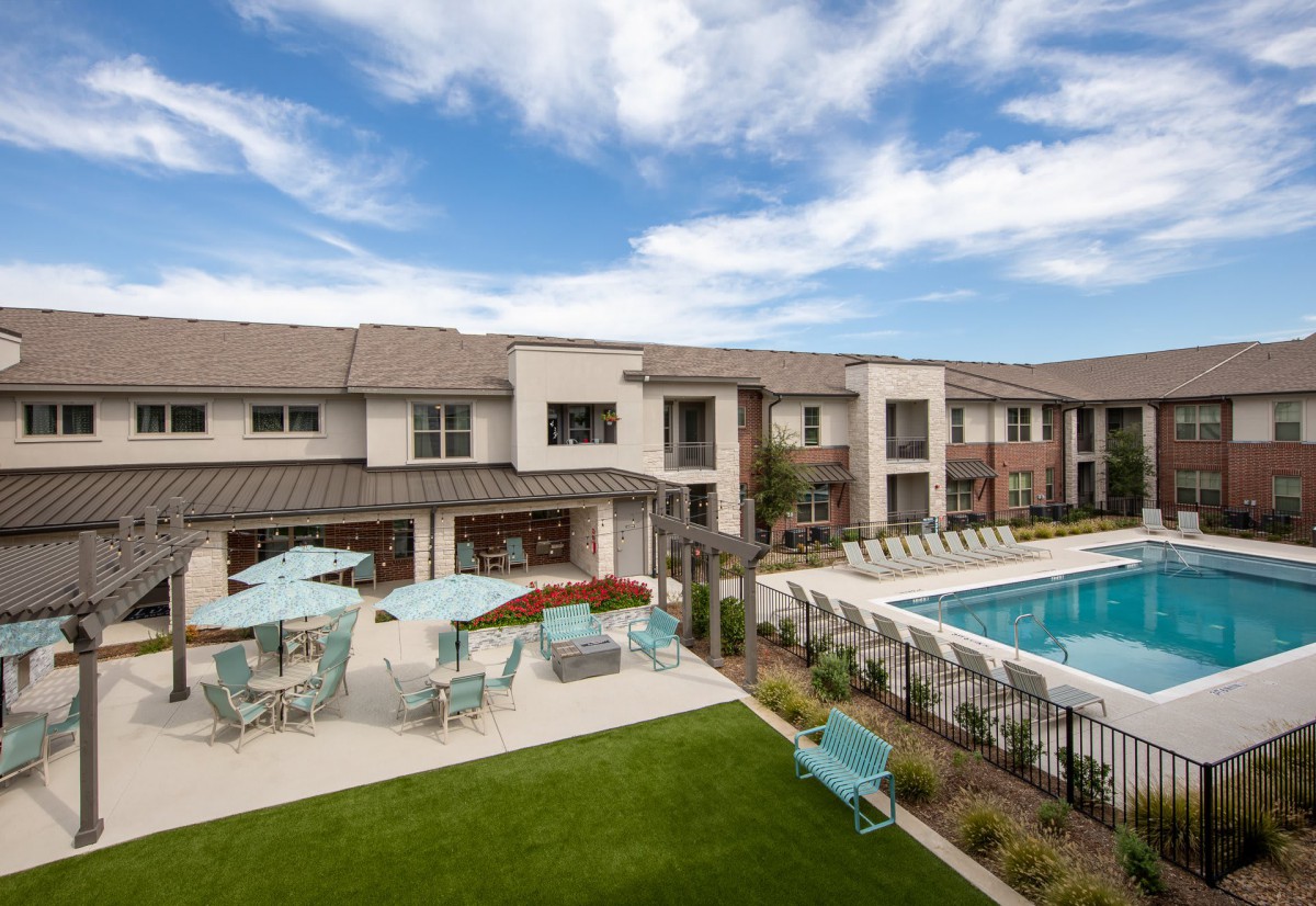A modern apartment complex featuring a pool and outdoor seating area, surrounded by well-maintained landscaping.