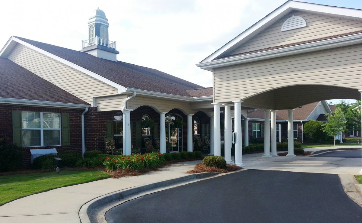 A building with a covered entrance and columns, surrounded by well-maintained landscaping.