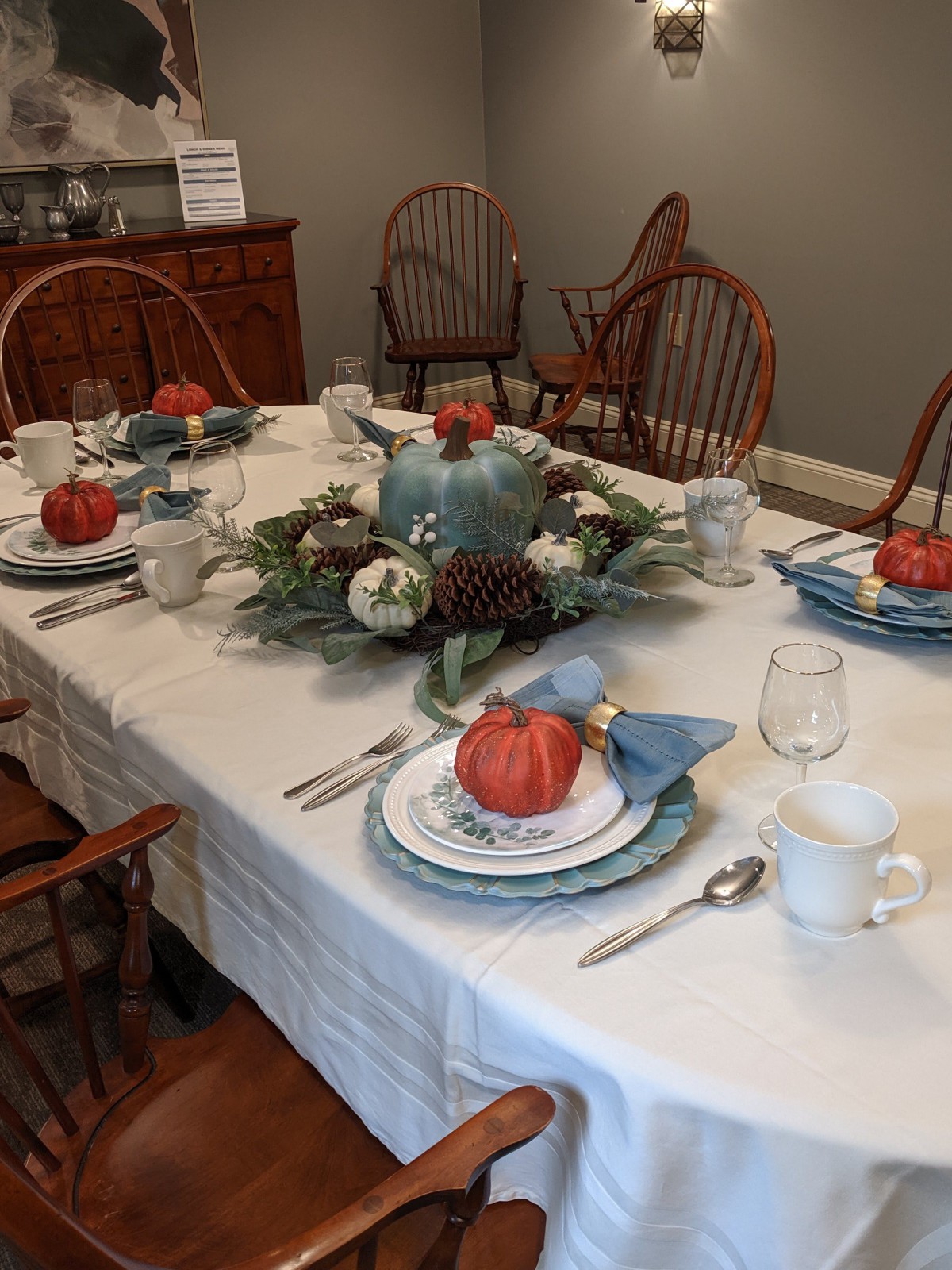 A dining table elegantly set with fall-themed decor, featuring pumpkins and a floral centerpiece.