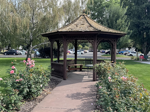 A charming wooden gazebo surrounded by blooming flowers in a peaceful park setting.