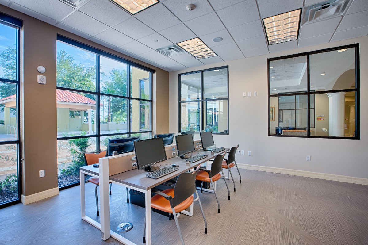 A modern office workspace with desks and computers, featuring large windows and ample natural light.