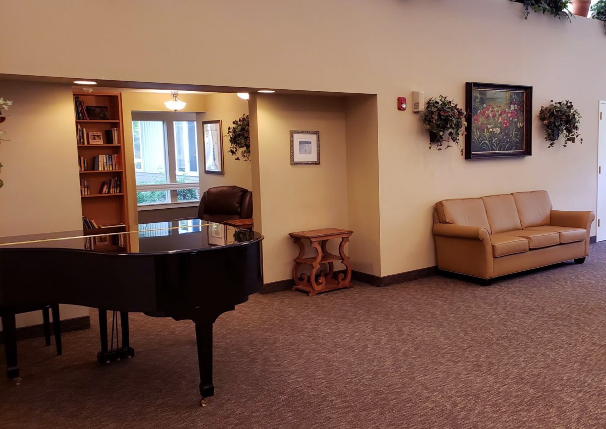 A cozy lobby area featuring a grand piano, bookshelf, and comfortable seating.