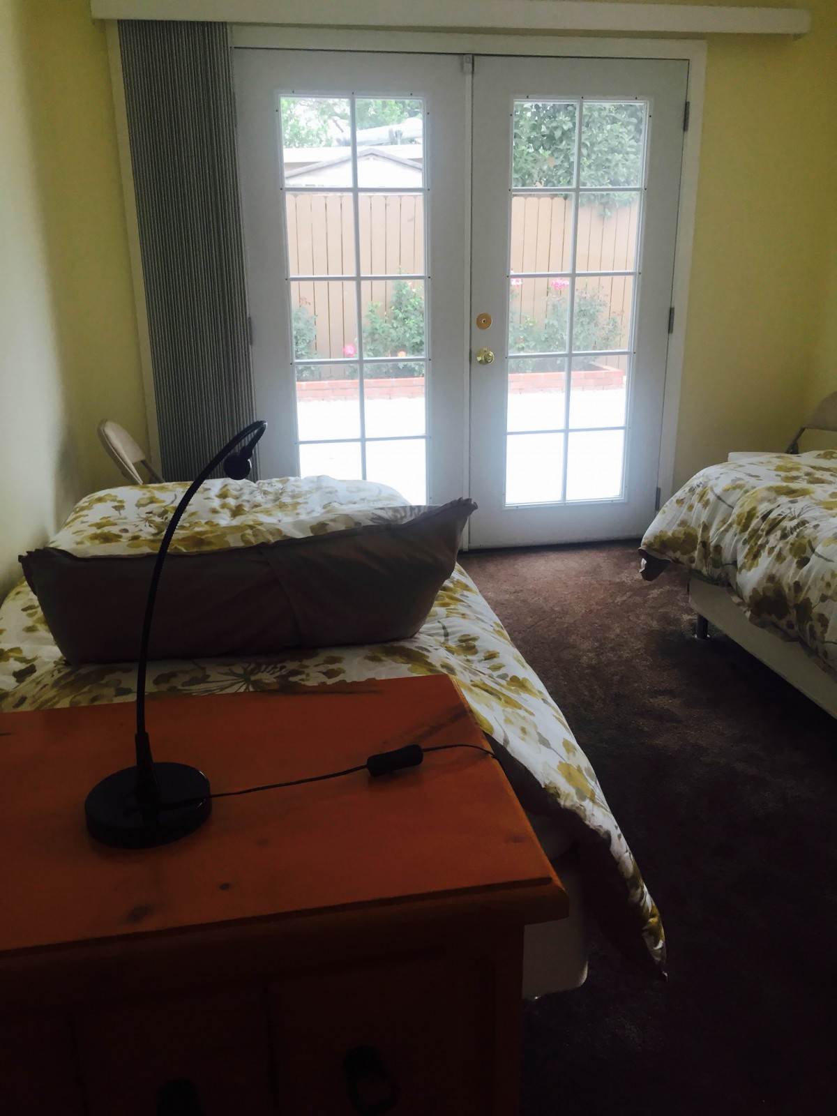 A cozy bedroom with twin beds and a desk lamp, featuring glass doors that allow natural light to fill the room.