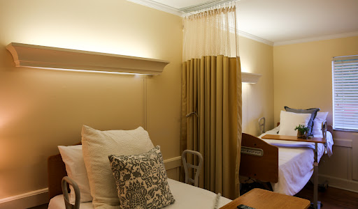 A serene hospital room featuring two beds adorned with decorative pillows and soft lighting.