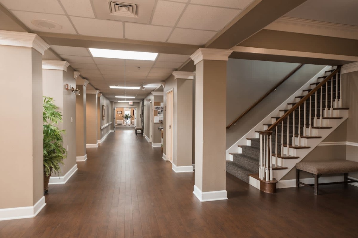 A spacious and well-lit hallway with wooden flooring, featuring stairs on the right.