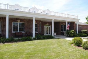 A single-story brick house with a white porch and neatly maintained lawn.
