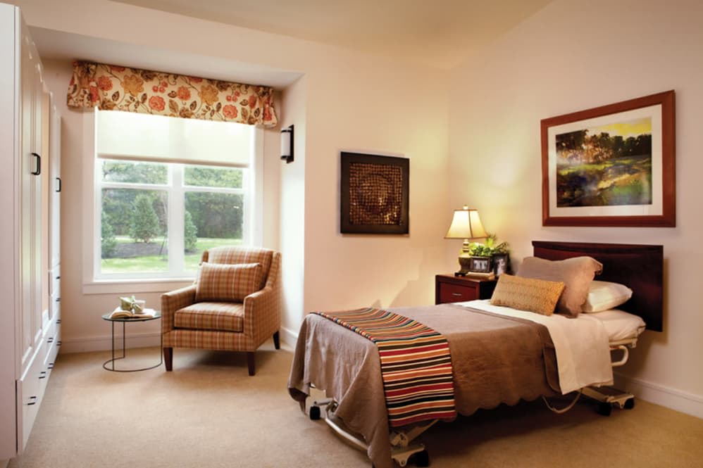 A cozy bedroom with a single bed, armchair, and large window.