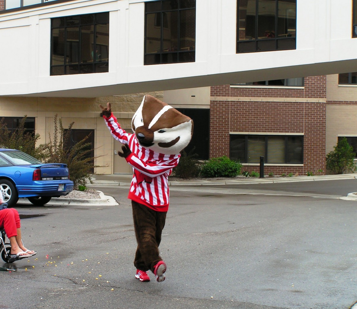 A person in a mascot costume wearing a striped shirt is standing outdoors on the street.