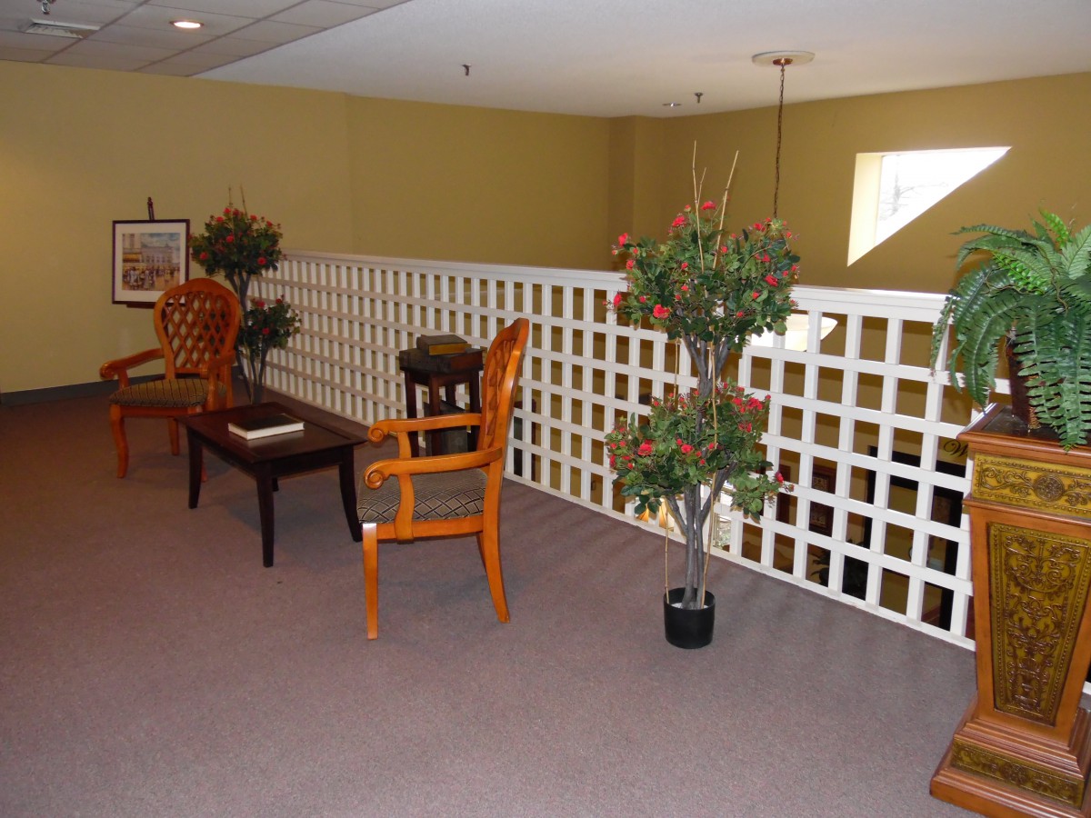 A cozy interior space featuring a wooden chair and table set, potted plants, and a white lattice railing.