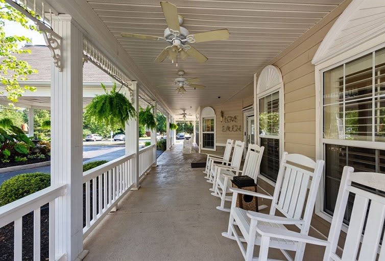 A cozy porch with white rocking chairs and ceiling fans, surrounded by lush hanging plants.