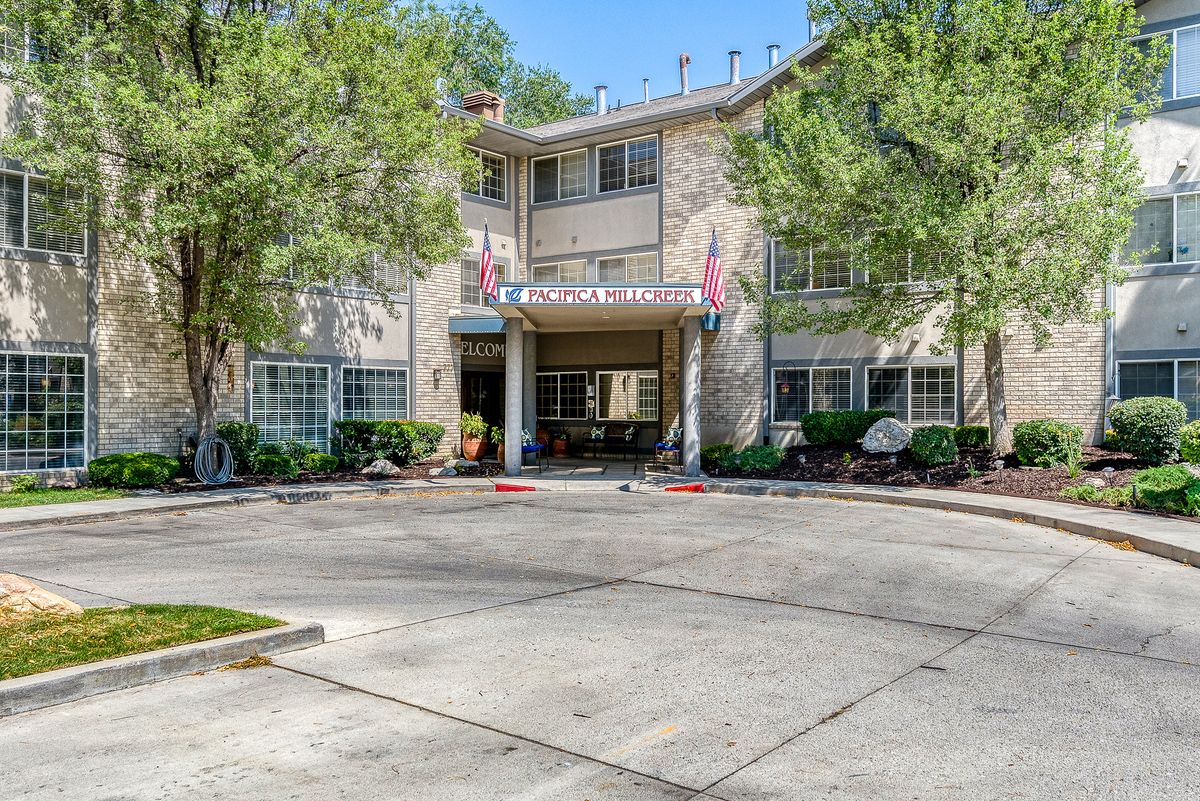 A view of an apartment complex entrance surrounded by trees and a driveway.