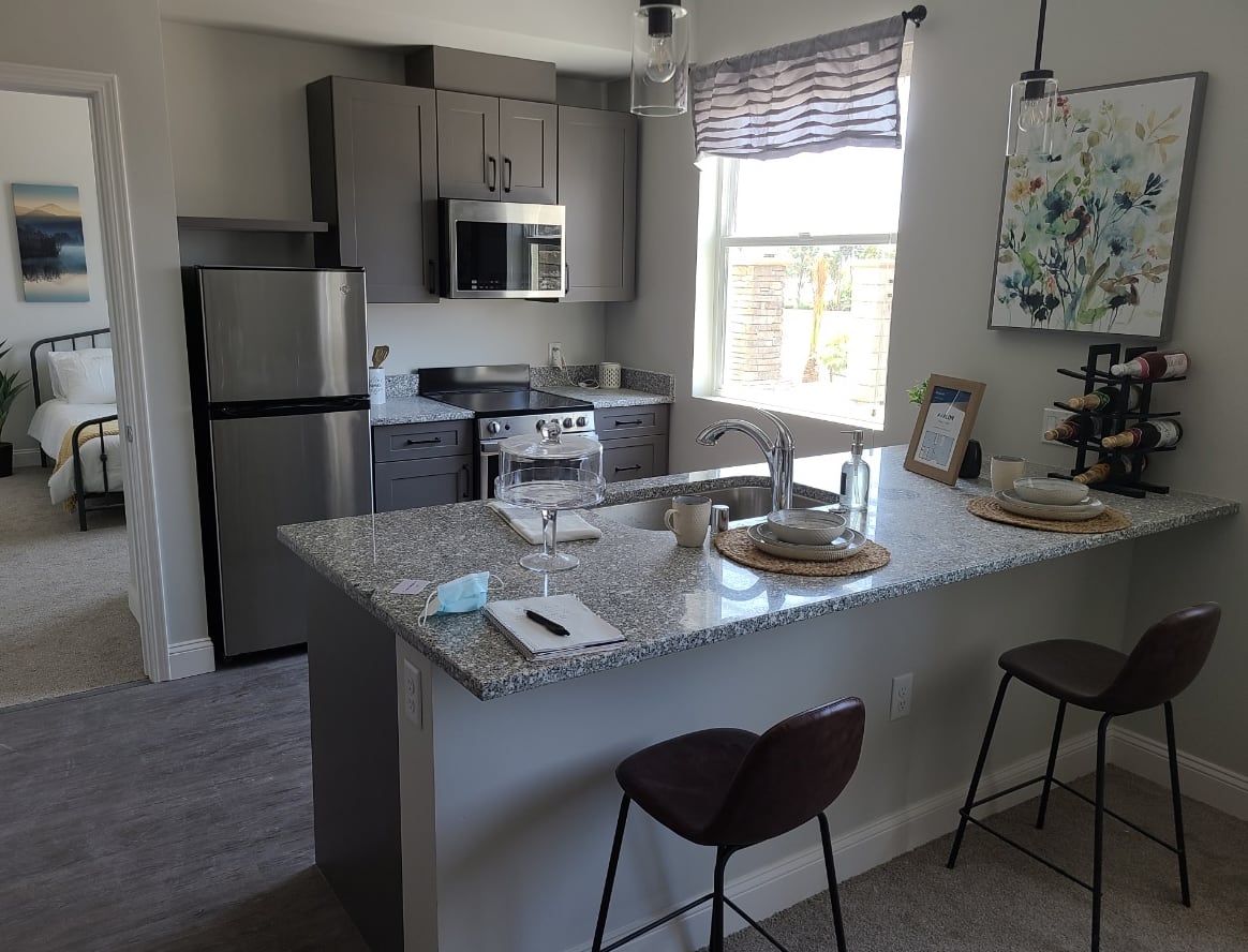 A modern apartment kitchen with stainless steel appliances and a sleek countertop with bar stools.