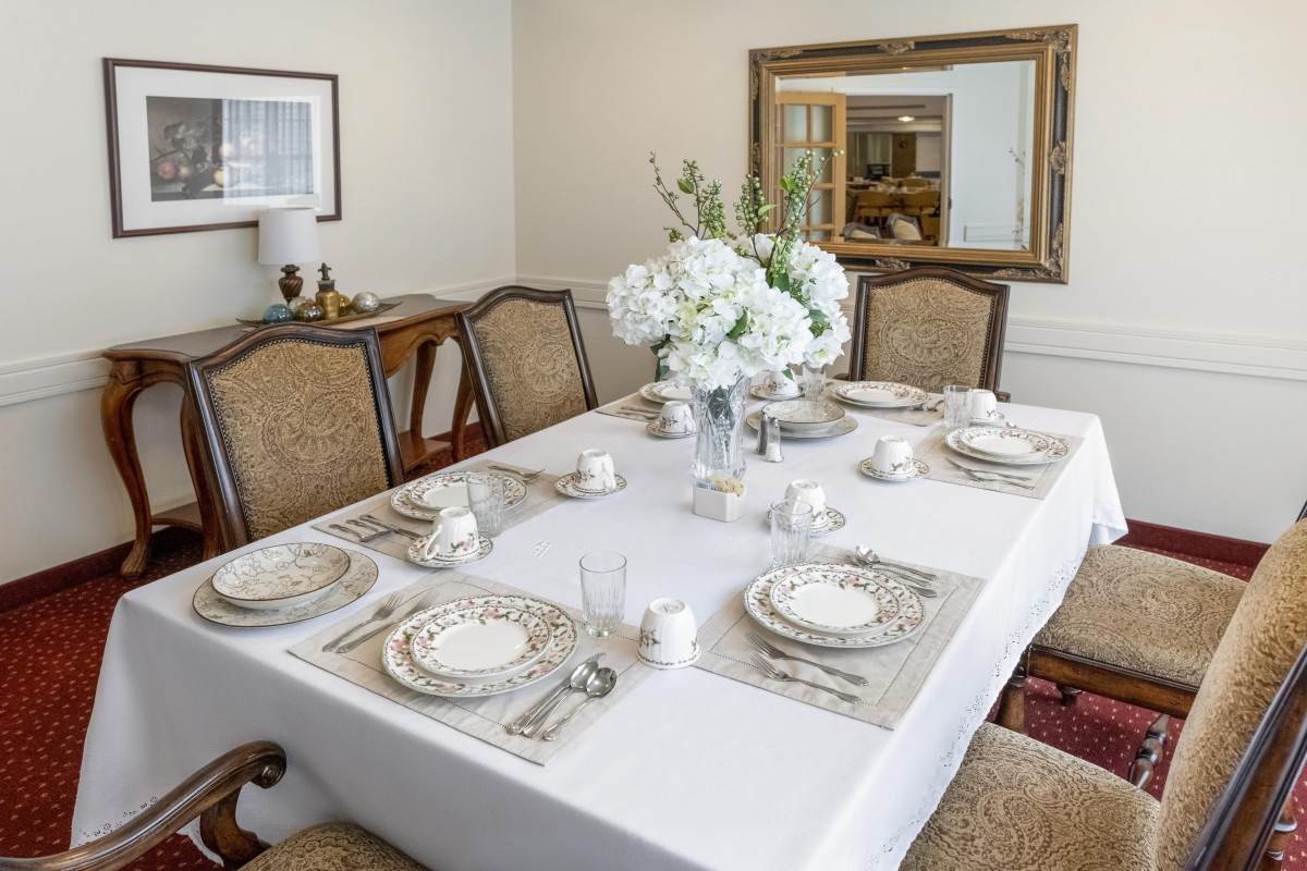 A beautifully set dining table with elegant dishware and a floral centerpiece in a well-decorated dining room.