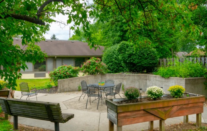A tranquil garden patio with lush greenery, featuring a seating area with a table and chairs.