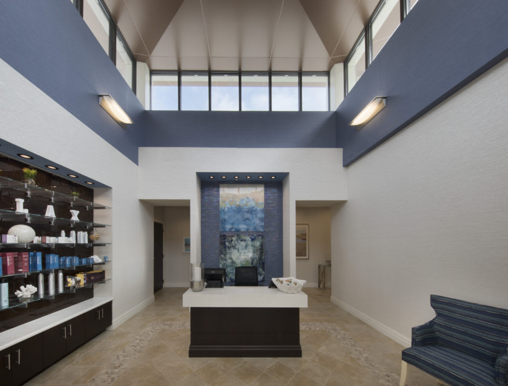 A modern reception area with a high ceiling, featuring a front desk, shelves with decorative items, and elegant furnishings.