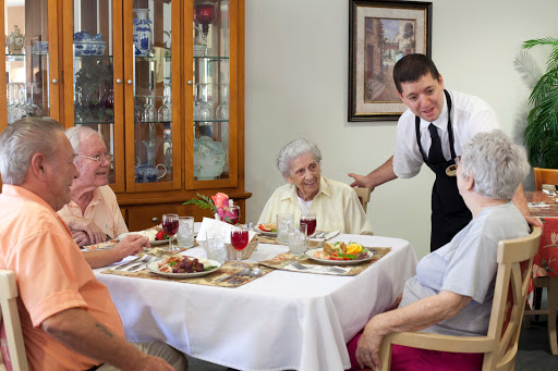 A group of elderly individuals enjoying a meal together, with a waiter serving at the table.