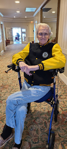 A senior individual in a black and yellow jacket seated in a wheelchair, enjoying the indoor environment.