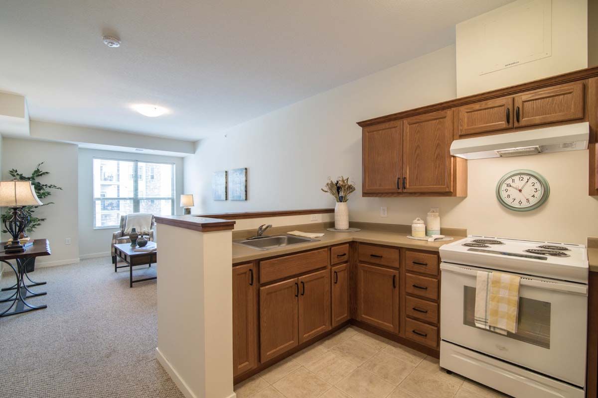A cozy apartment kitchen with wood cabinets and an open layout leading to a bright living area.
