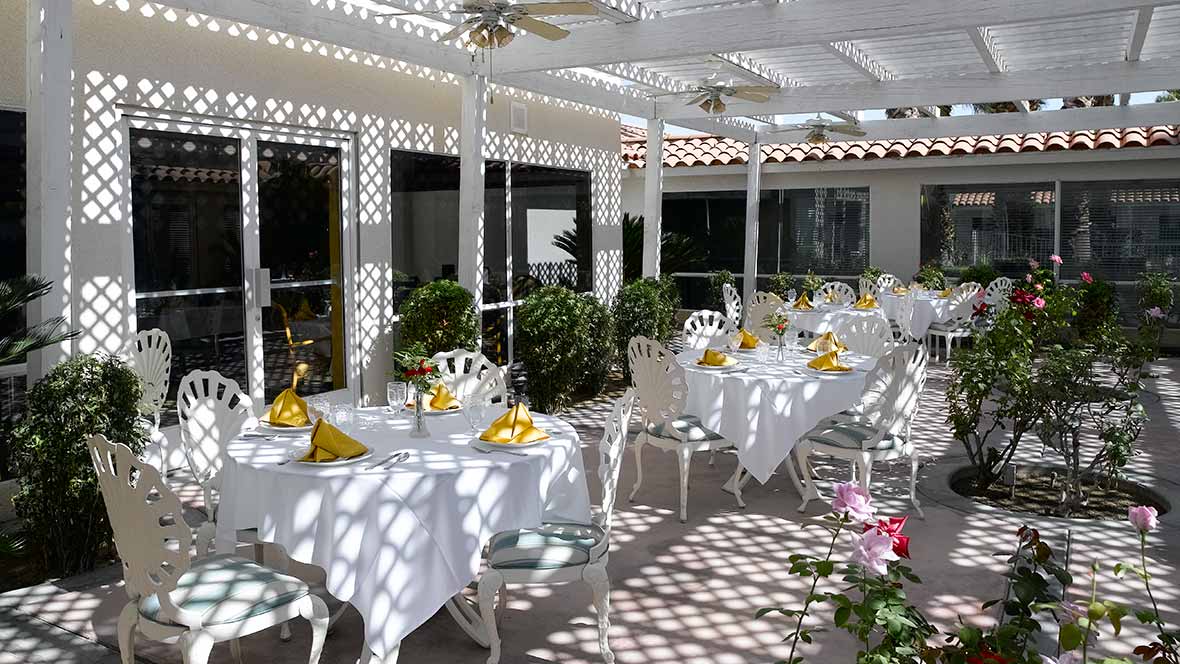 A beautifully set outdoor dining area with tables adorned with yellow napkins under a pergola.