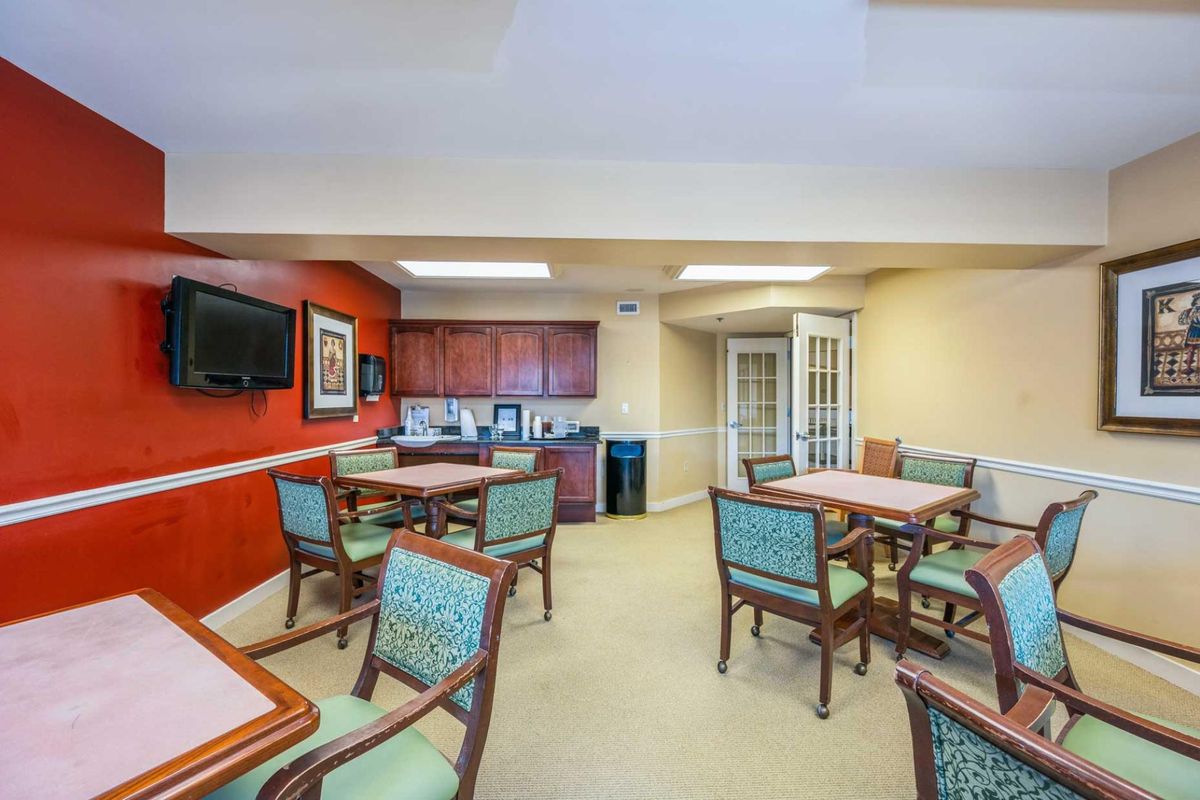 A cozy dining area with multiple tables and chairs, featuring a kitchenette and a television.