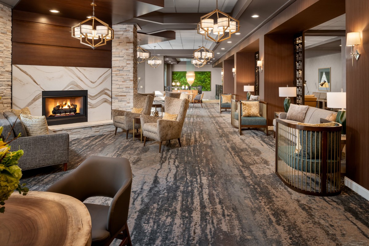 A modern hotel lobby featuring a cozy seating area with a fireplace and elegant chandeliers.