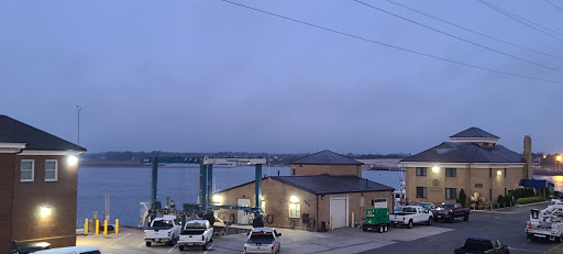 A quiet harbor scene at dusk, featuring a range of vehicles and a building near the water.