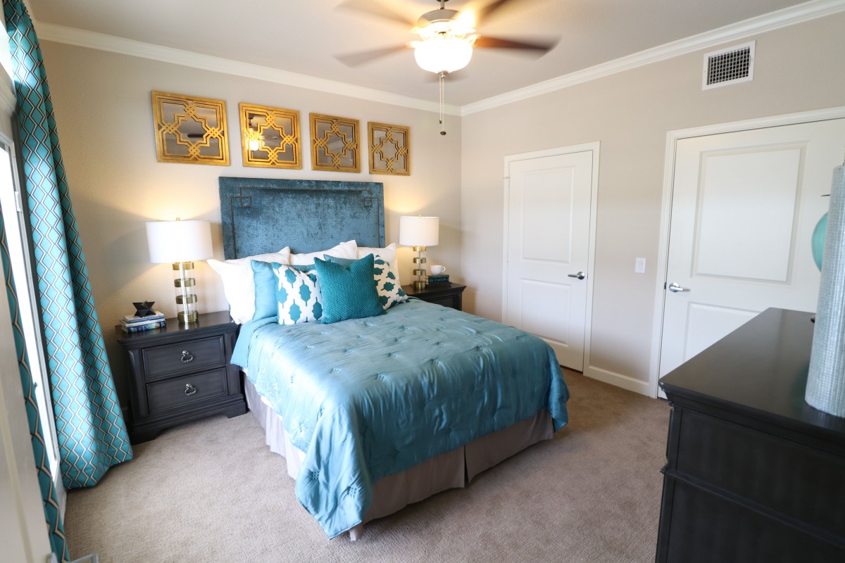 A cozy bedroom with a blue and white color scheme, featuring a neatly made bed, bedside lamps, and wall artwork.