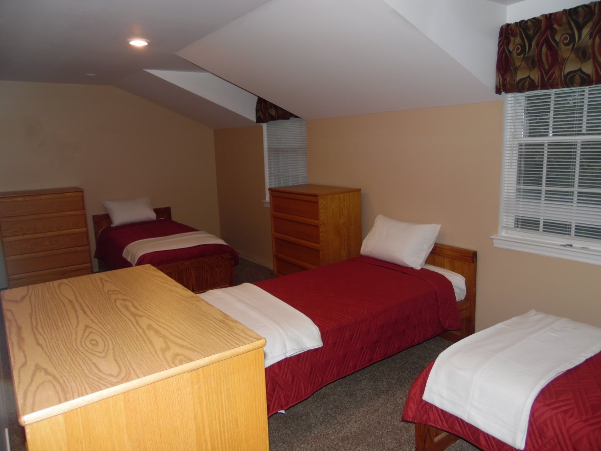 A bedroom with three single beds and wooden furniture.