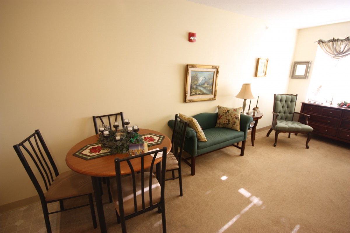 A cozy living room with a dining table, chairs, and a sofa, complemented by artwork and soft lighting.