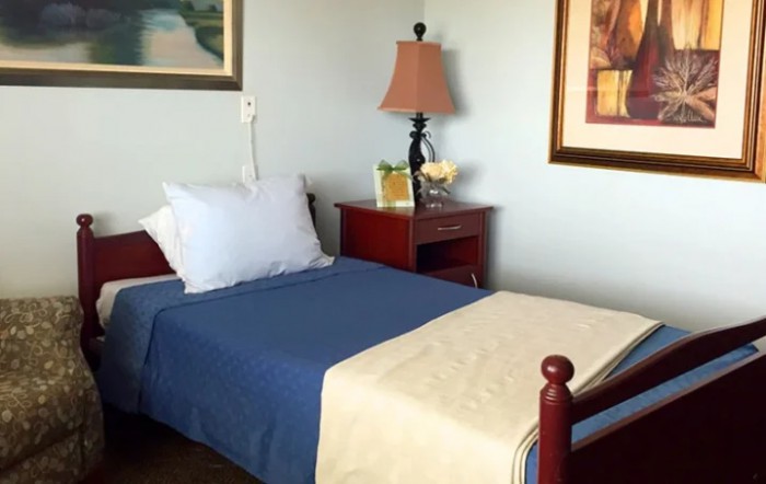 A cozy bedroom with a single bed, blue bedding, and a nightstand featuring a lamp and decor.