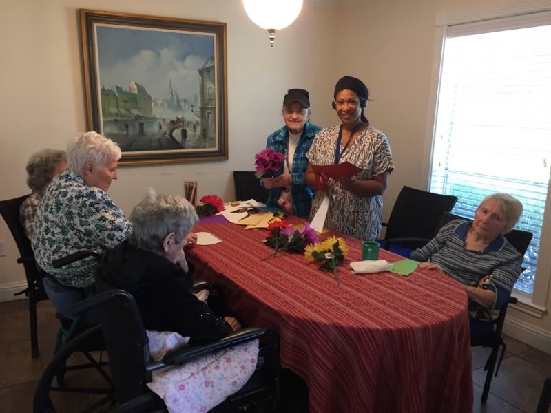 A group of people gathered around a table in a cozy indoor setting, engaging in a social activity with flowers and crafts.