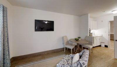 A modern minimalist living area with a wall-mounted television and a small dining table with chairs.