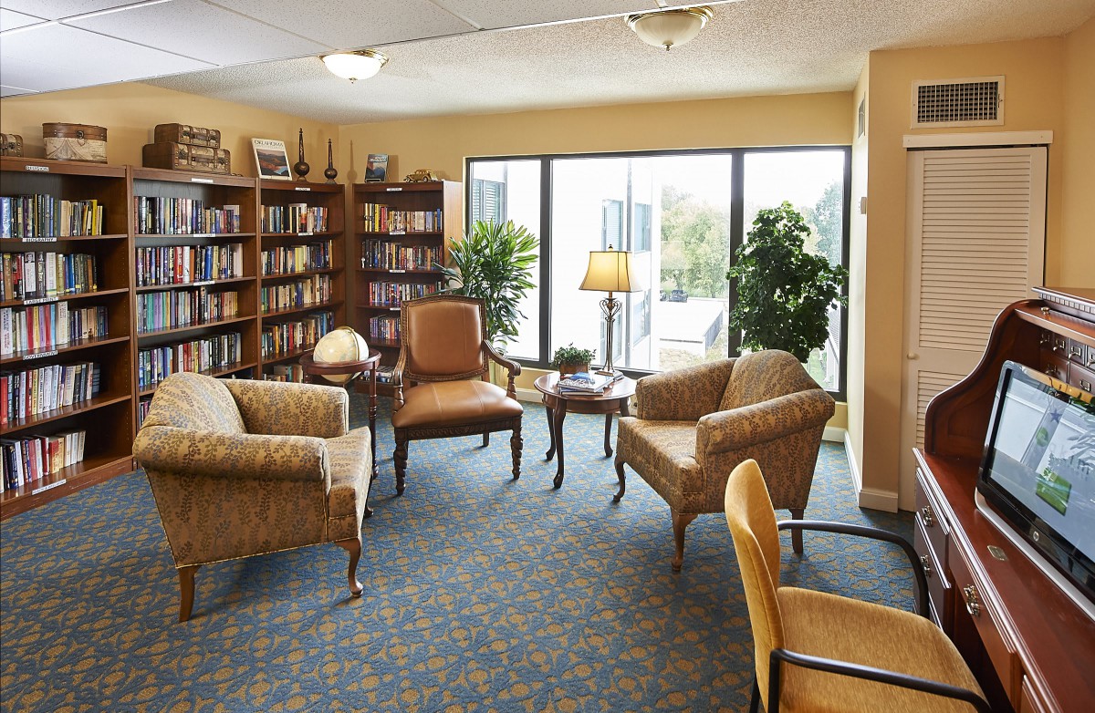 A cozy library room with armchairs, bookshelves, and natural light.