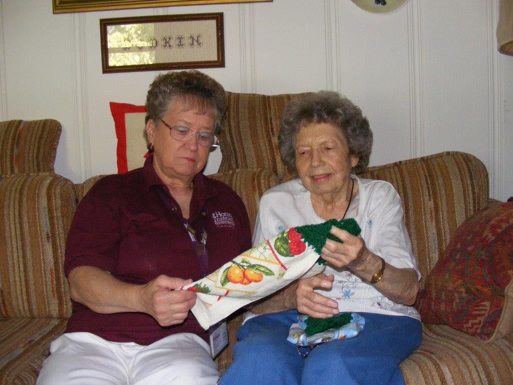 Two older adults sitting on a sofa, engaging in a craft activity indoors.