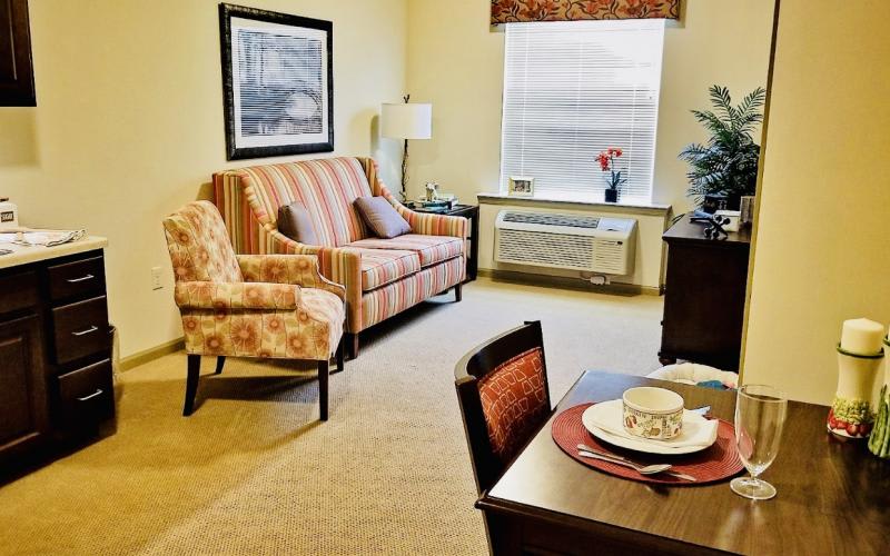 A cozy living room with a sofa, armchair, and dining table set near a window.