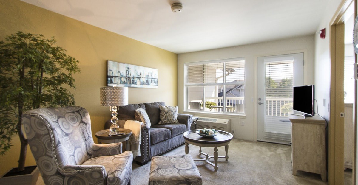 A cozy living room with a sofa, armchairs, and a coffee table near a window that lets in natural light.