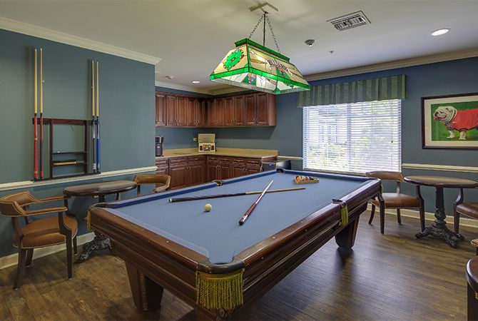 A cozy billiard room featuring a pool table, cue sticks, and a stained glass hanging light.