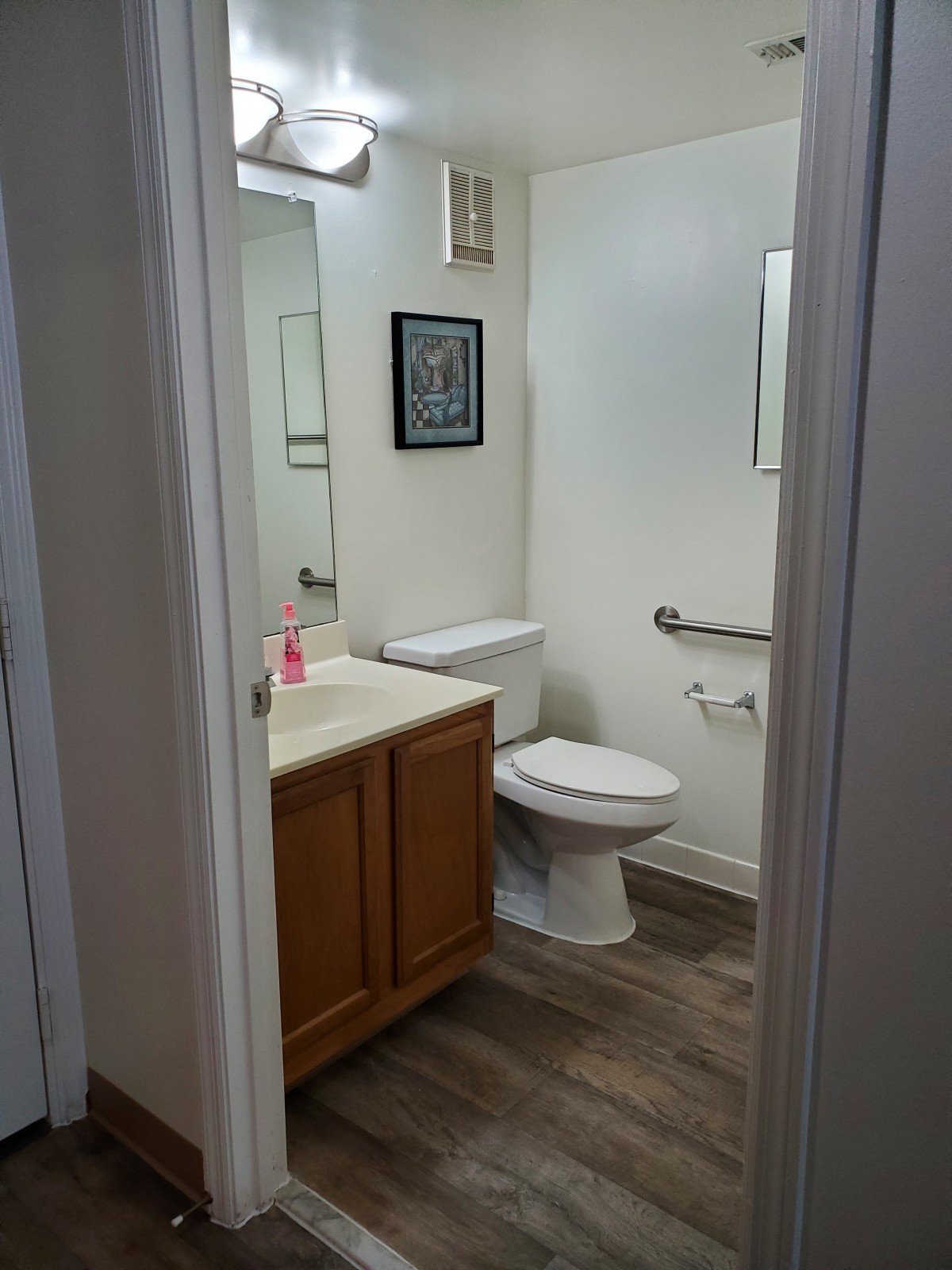A modern bathroom featuring a toilet, sink, and mirror with decorative wall art.