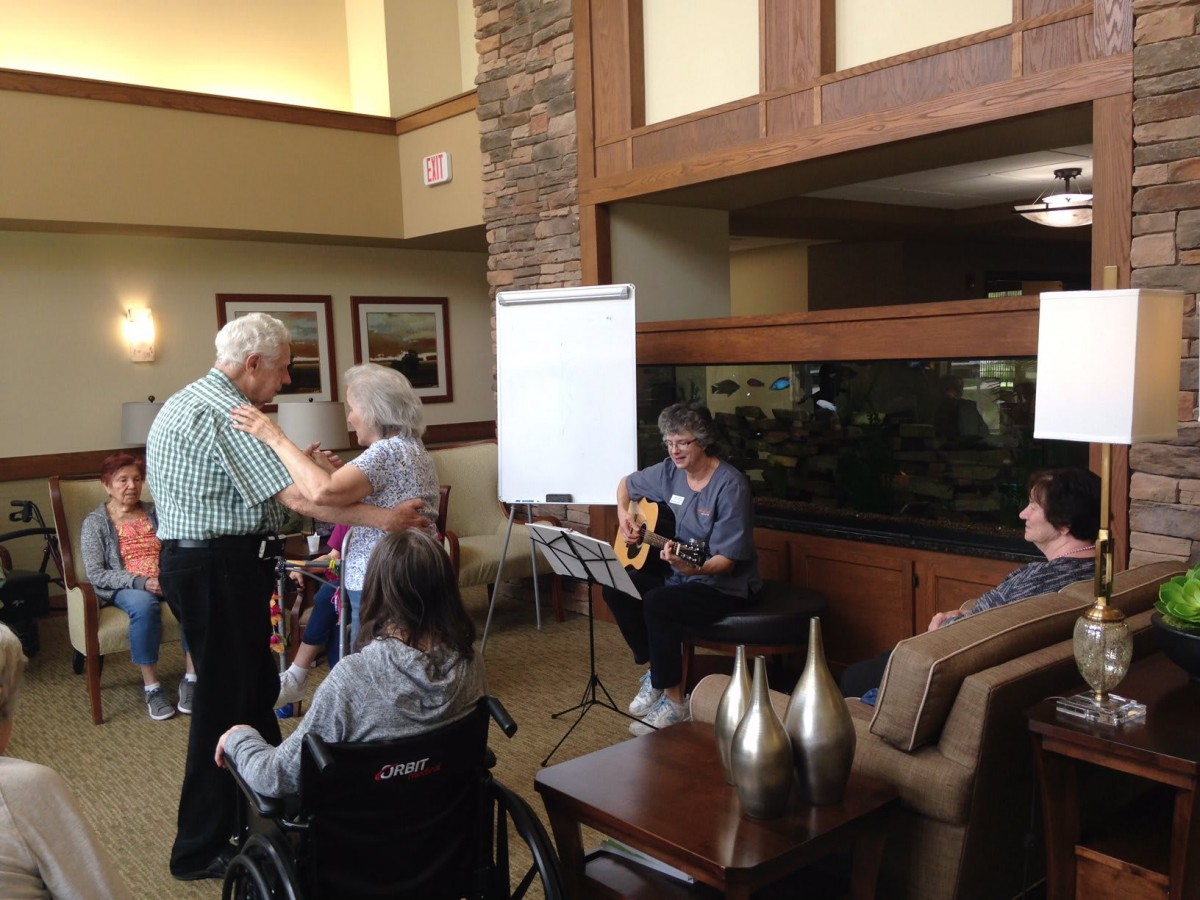 Elderly residents enjoy music and dancing in a nursing home setting.
