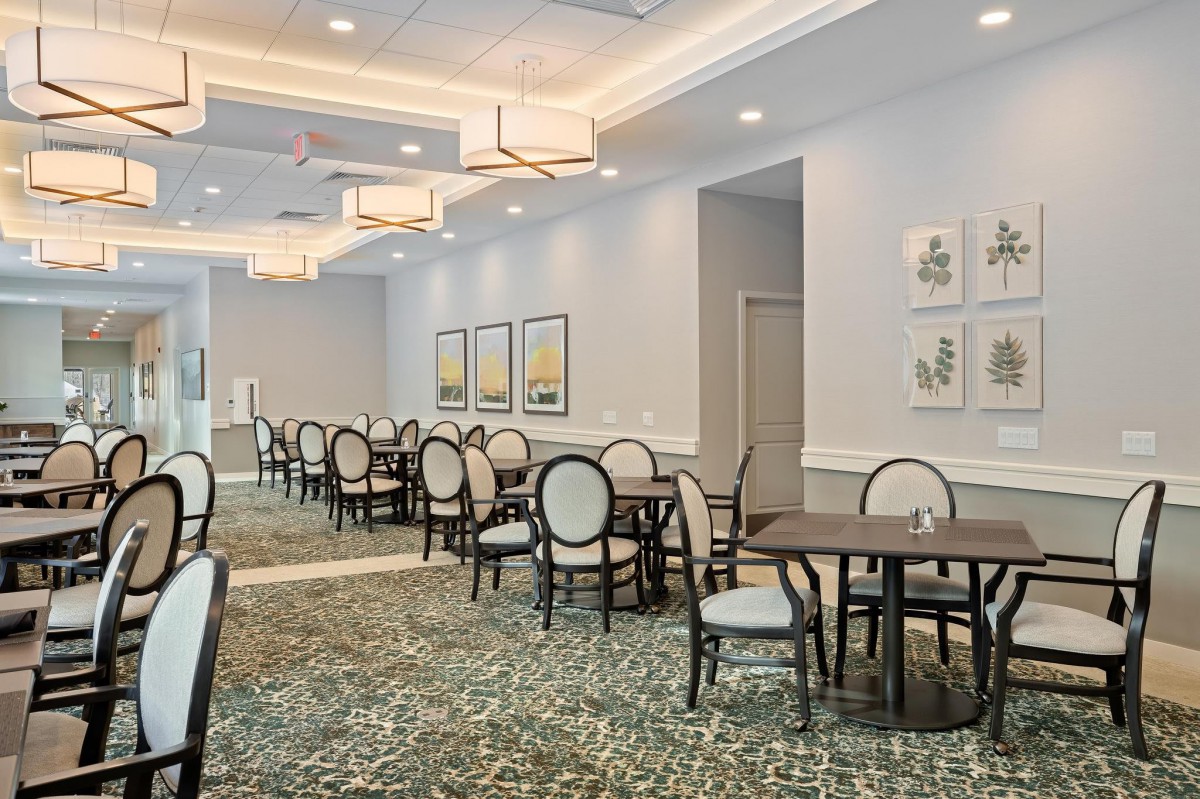A spacious dining room with neatly arranged tables and chairs, decorated with elegant artwork and bright lighting.