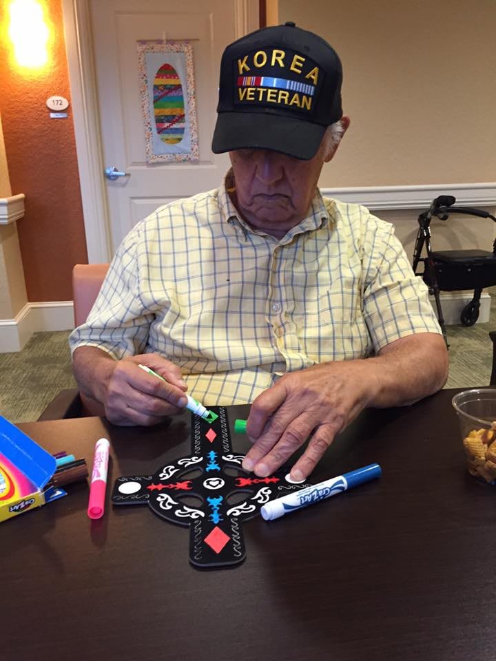 An elderly man wearing a veteran hat is engaged in playing a board game with markers on the table.