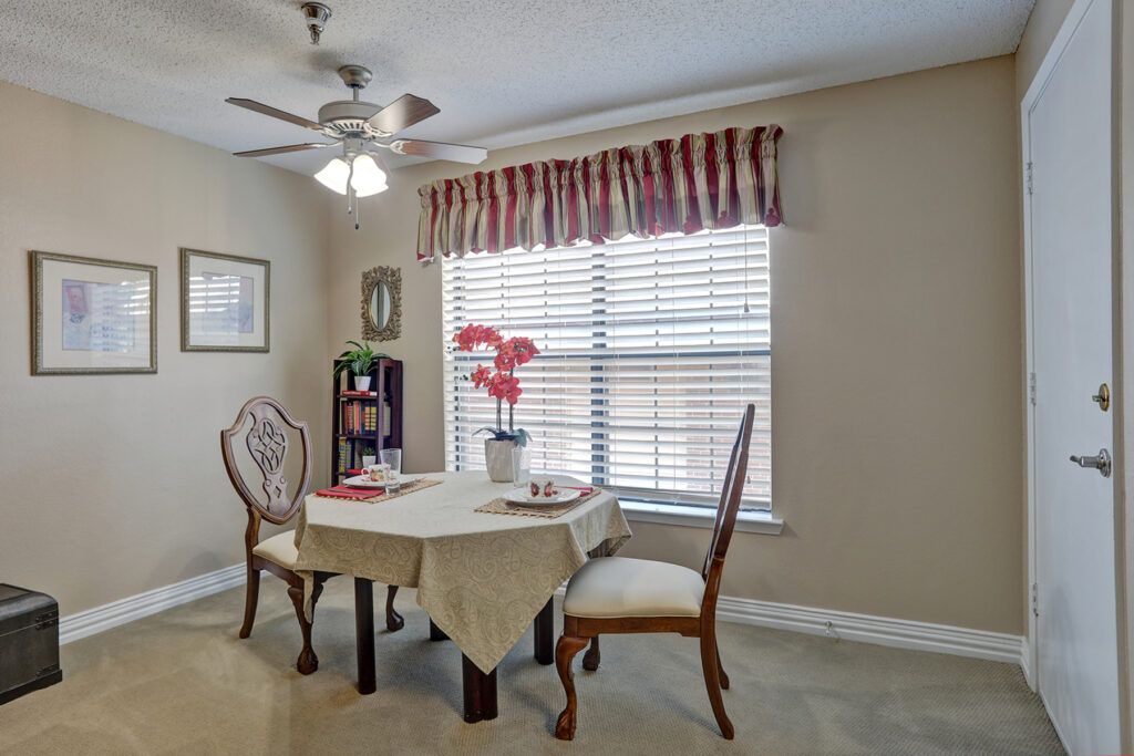 A cozy dining area with a table and two chairs, featuring a window with curtains and decorative elements.