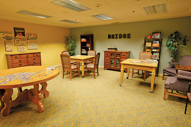 A cozy library reading room with tables, chairs, and bookshelves.